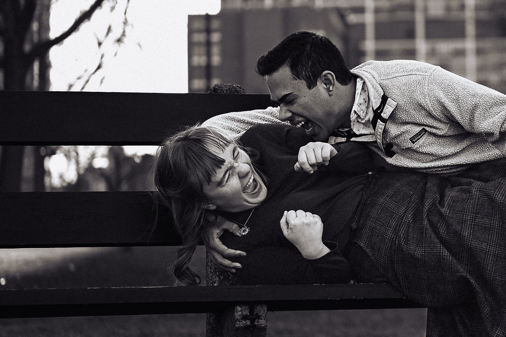 engaged couple tackling each other on a park bench in Los Angeles
